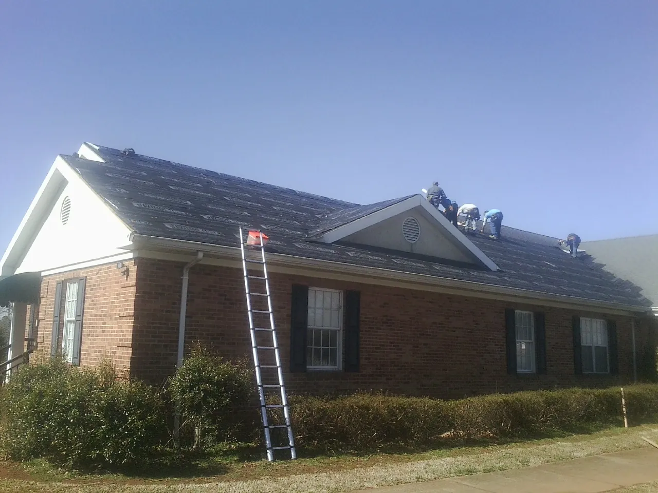 Crew tearing shingles off a brick ranch roof with a ladder set — Metal Roof Repair work by our crew in Selma